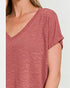 Close-up of a person wearing a pinkish-red short-sleeve top against a light gray background