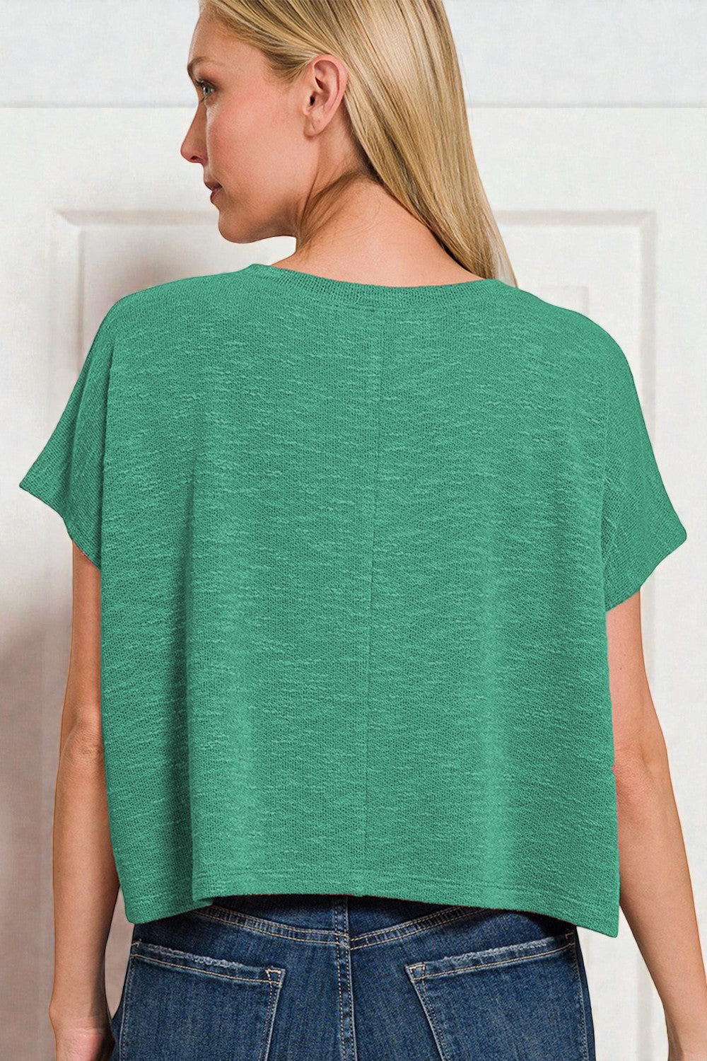 Woman wearing a green top and blue jeans against a white background