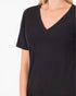 A close-up of a person wearing a plain black short-sleeve V-neck top against a light gray studio background.