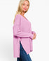 A woman wearing a lavender purple knit sweater with a V-neck and textured ribbed sleeves, paired with blue jeans, photographed against a plain white studio background.