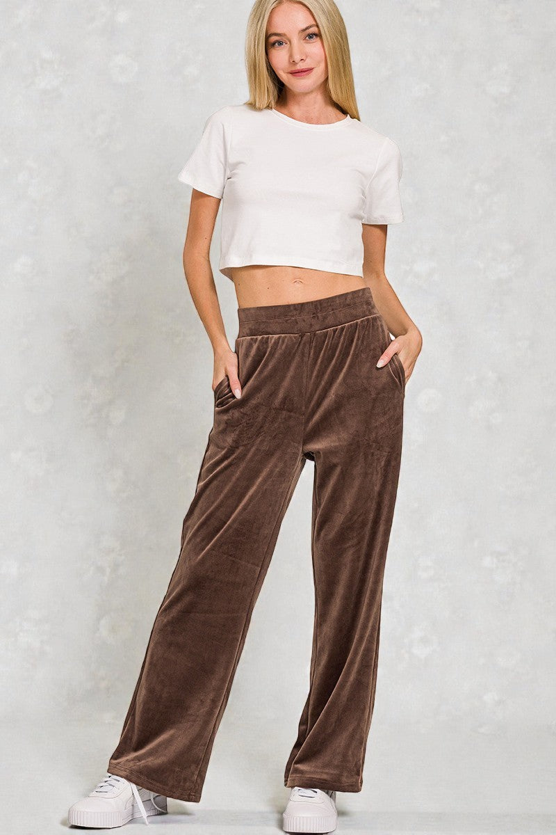 Woman wearing a white crop top and brown velvet pants against a light gray background