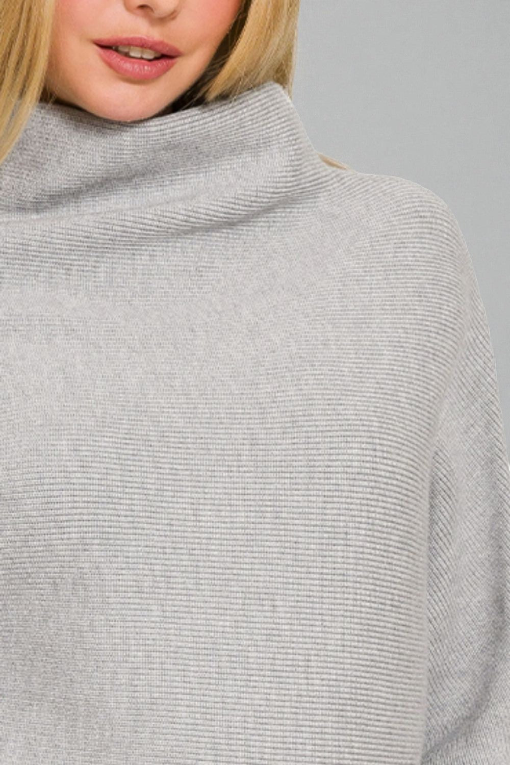 Close-up of a person wearing a gray ribbed sweater against a neutral background