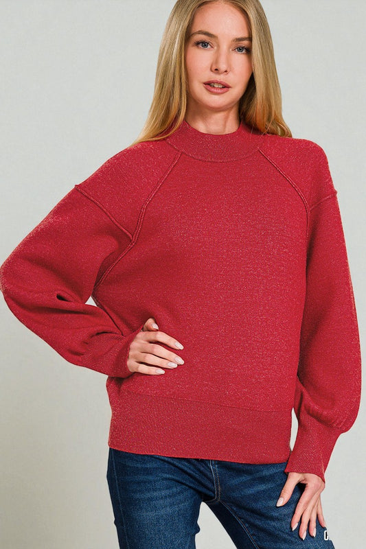 Woman wearing a red sweater and blue jeans against a plain background