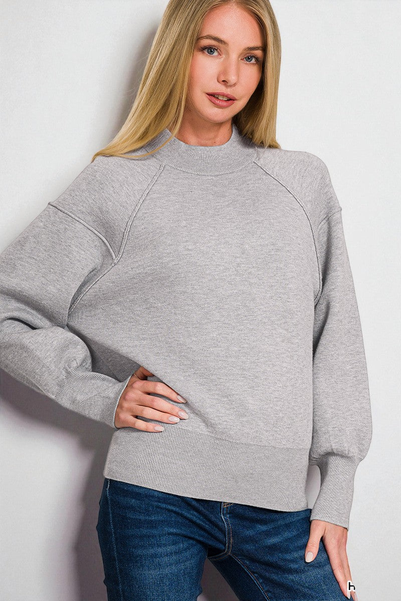 Woman wearing a gray sweatshirt and blue jeans against a white background