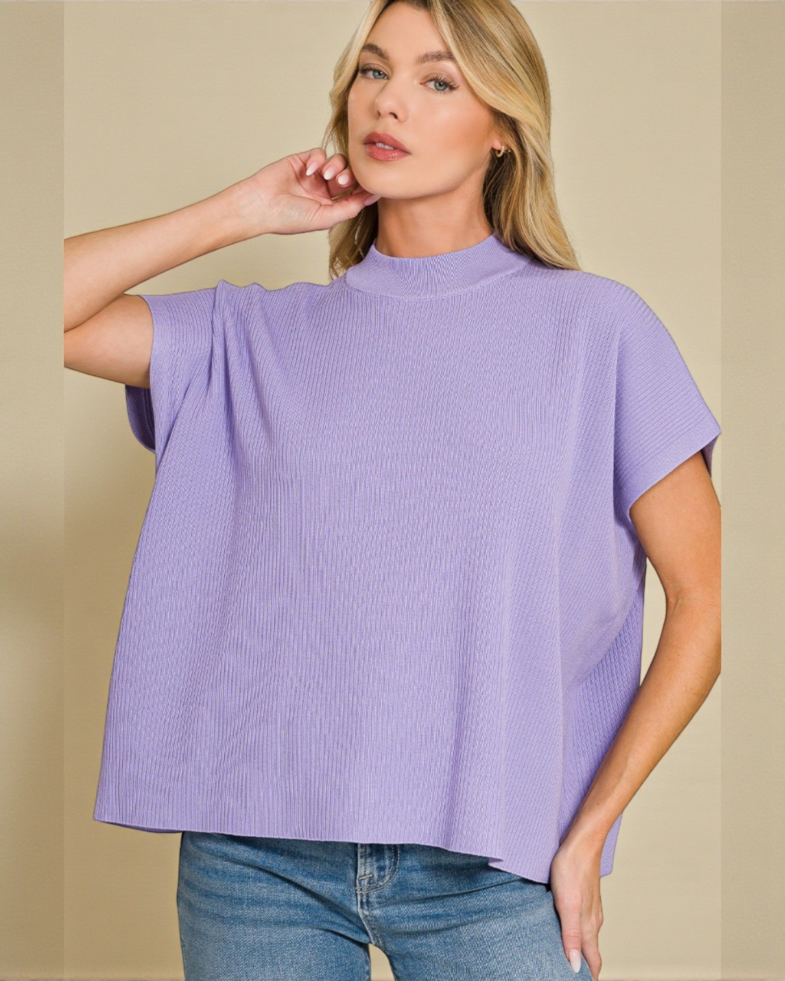 Woman wearing a purple top and blue jeans against a beige background