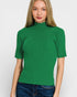 Woman wearing a green ribbed turtleneck sweater against a white background