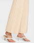 White high-heeled sandals worn with beige pants on a light gray background