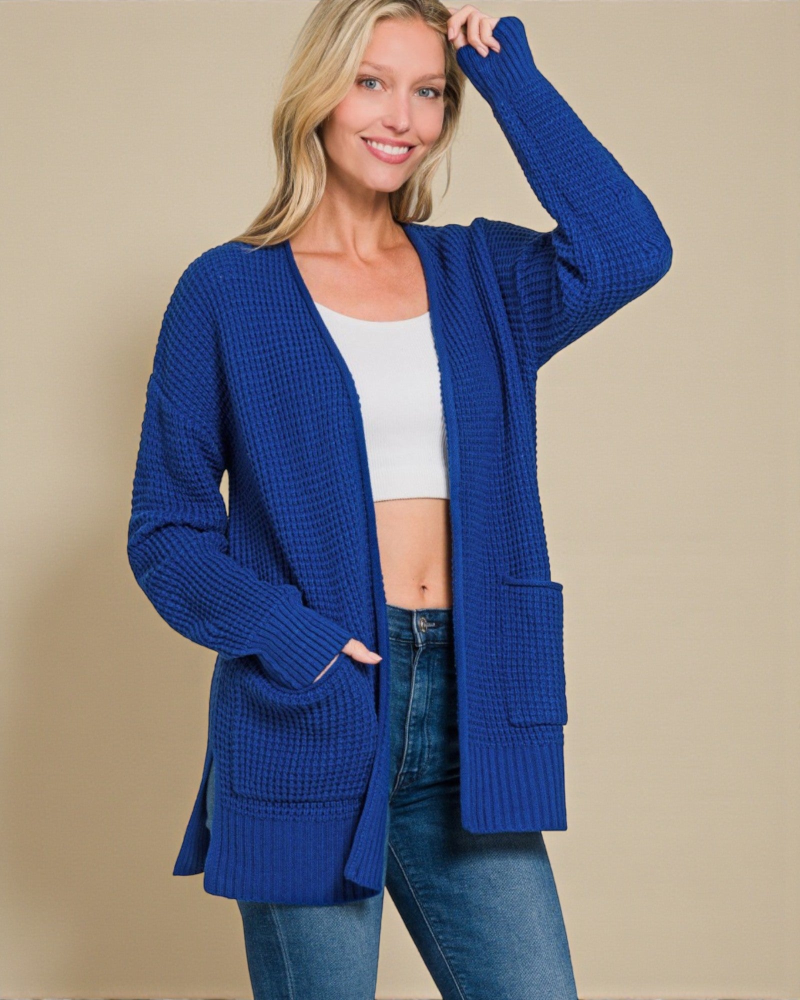 Woman wearing a blue cardigan over a white top and jeans on a beige background