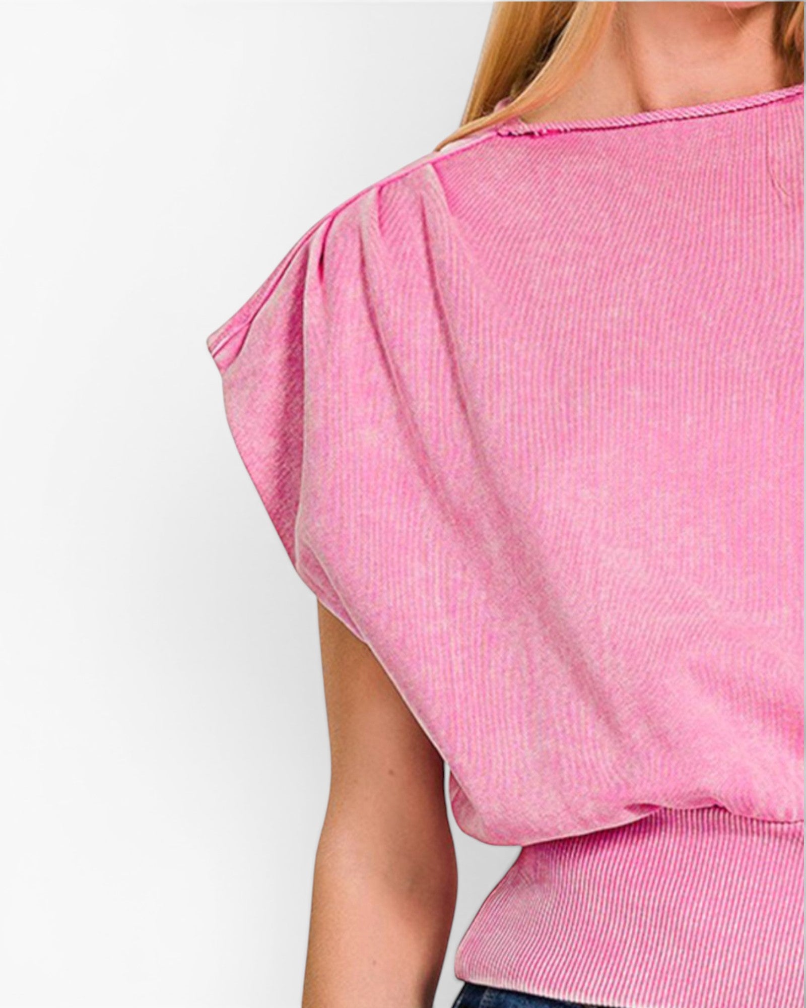 A close-up of a person wearing a pink ribbed knit top with a wide boat neckline and voluminous draped short sleeves, shown against a plain light background.