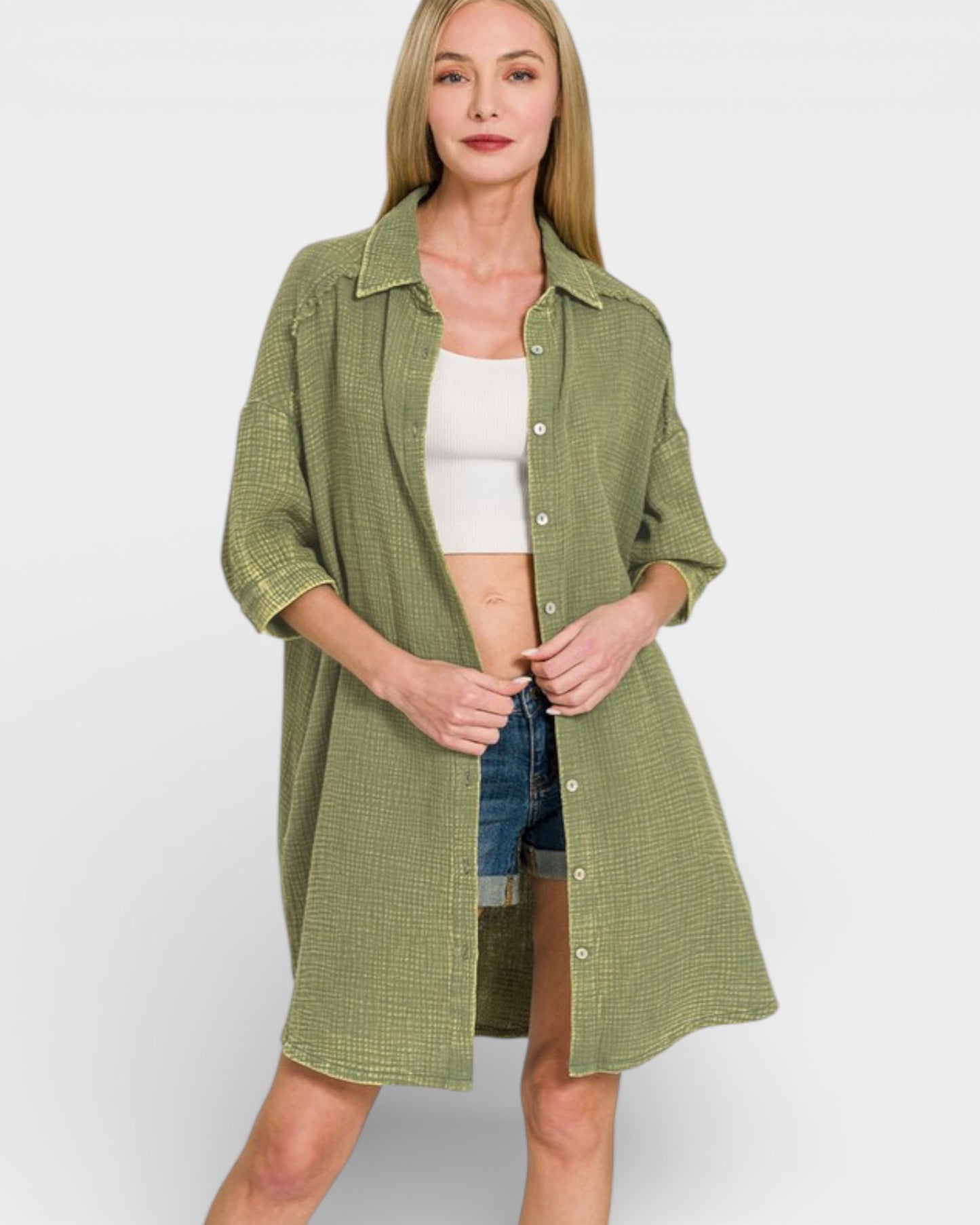 Woman wearing a green checkered shirt over a white top and denim shorts on a light gray background