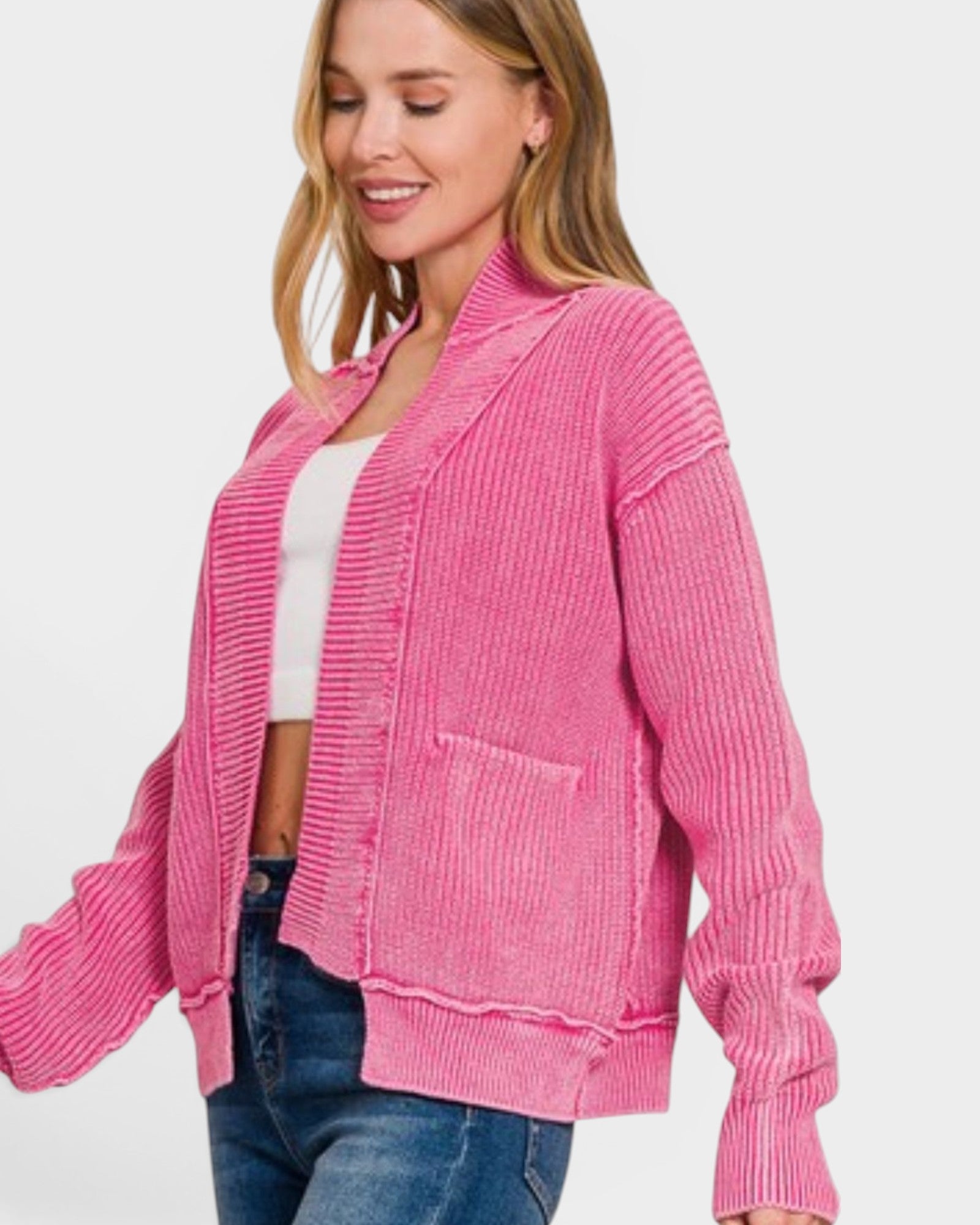 Woman wearing a pink cardigan over a white top and blue jeans on a light gray background