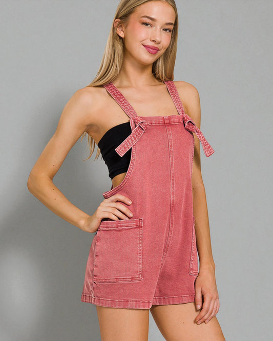 Woman wearing a pink denim pinafore dress against a gray background