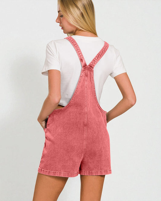Person wearing a pink denim overall dress with a white shirt underneath on a plain background