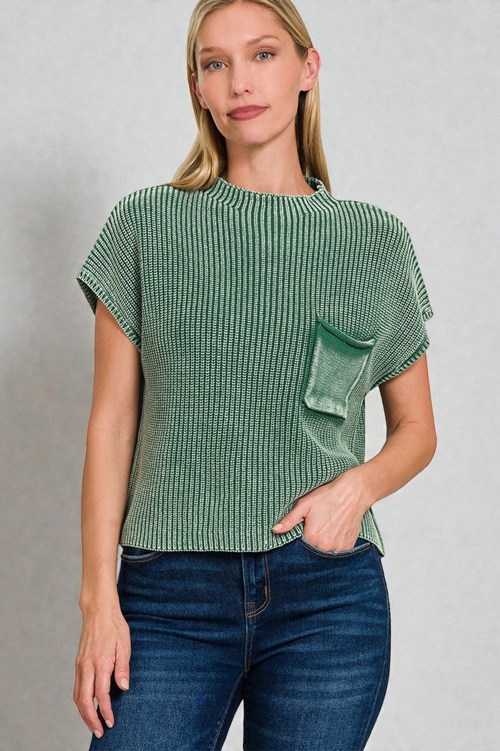 Woman wearing a green textured top with a pocket on a gray background