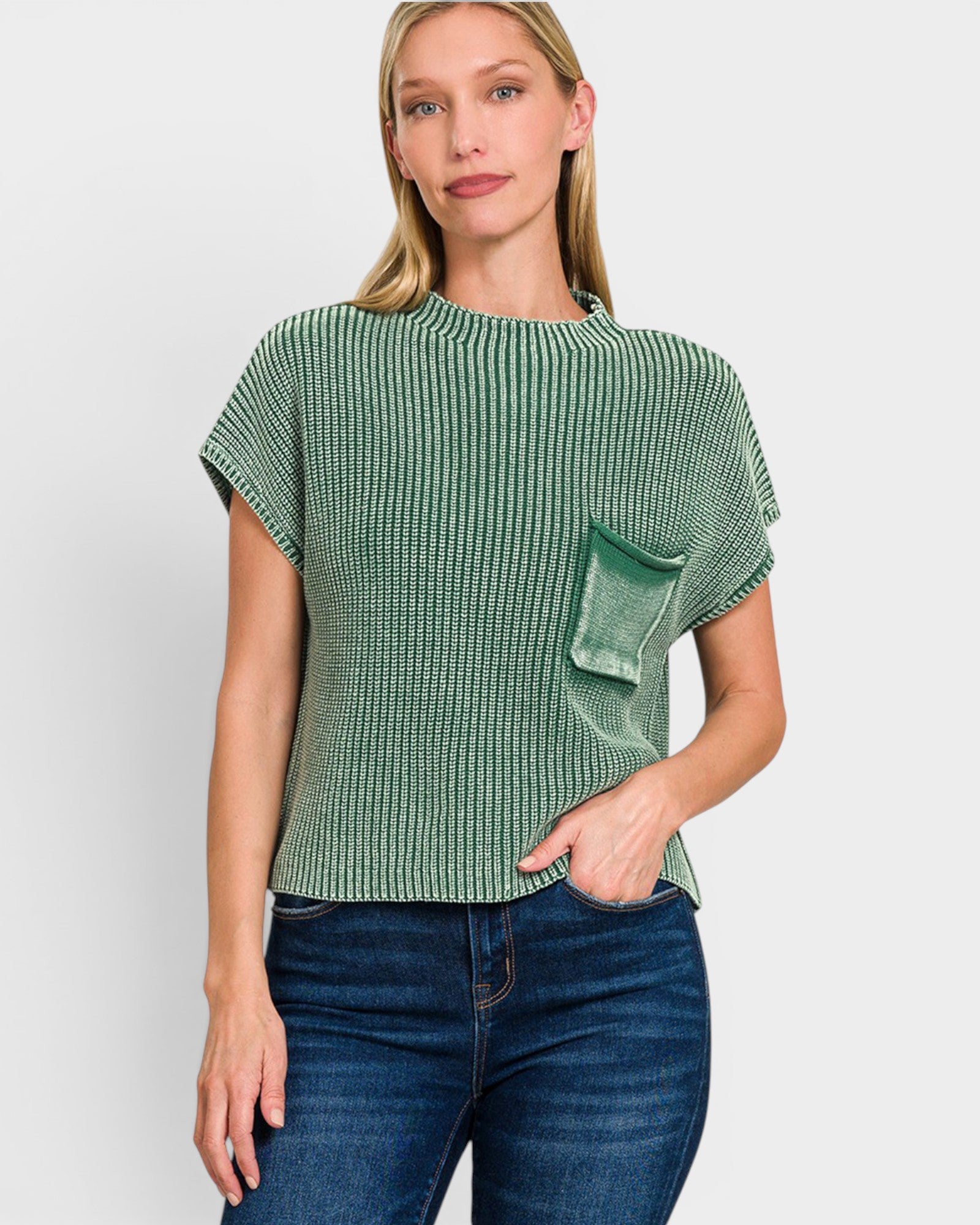 A woman modeling a green and white vertically striped short-sleeve knit top with a slouchy fit and a matching green pocket on the front, paired with dark blue jeans against a light gray background.