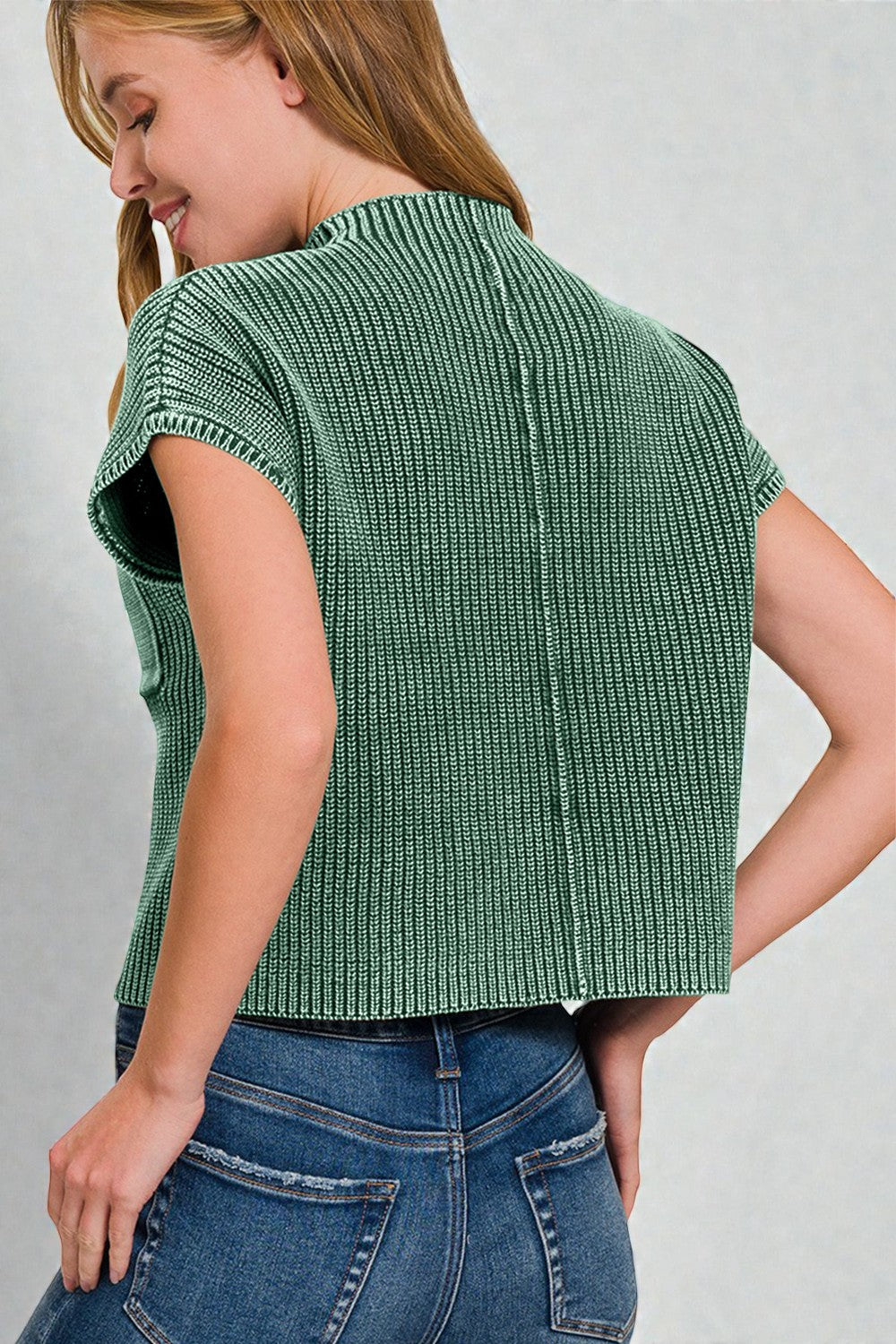 Woman wearing a green ribbed knit top against a gray background