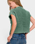 A woman wearing a green ribbed short-sleeve crop top and blue jeans, shown from a back-three-quarter angle against a light gray studio background.