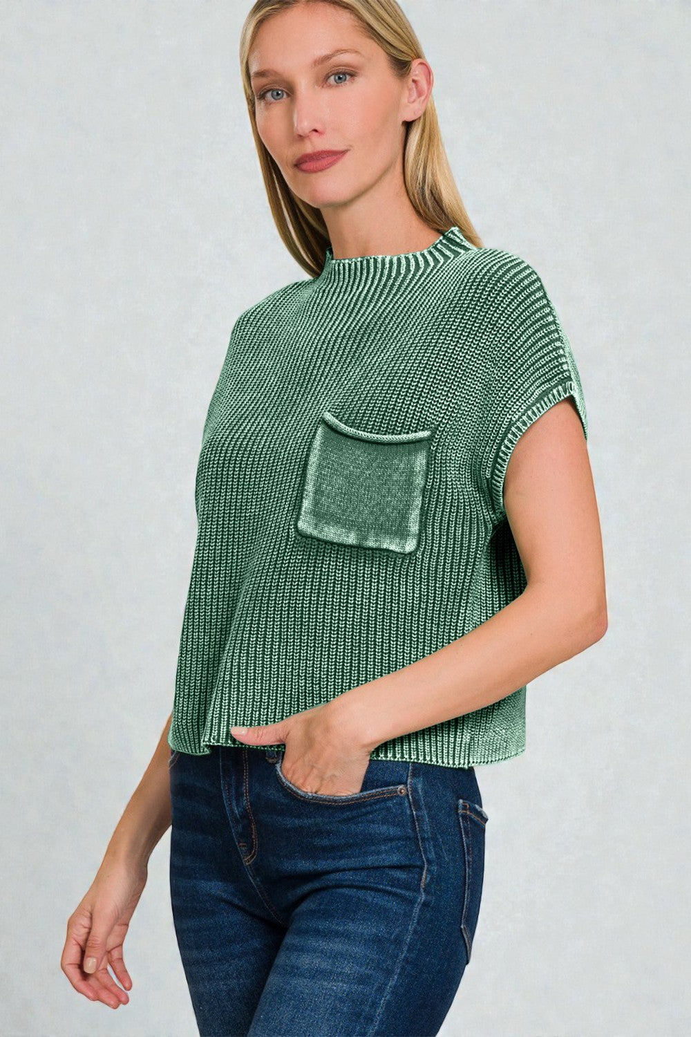 Woman wearing a green knitted top with a pocket on a plain background