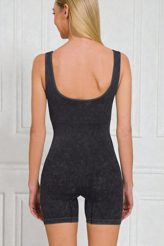 Person wearing a black ribbed tank top and shorts set against a white paneled wall.