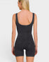 A woman shown from the back wearing a dark charcoal gray ribbed one-piece romper with shoulder straps and mid-thigh shorts, against a light gray studio background.