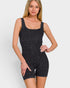 A woman modeling a dark gray ribbed tankini-style one-piece swimsuit with attached biker shorts against a light gray studio background.