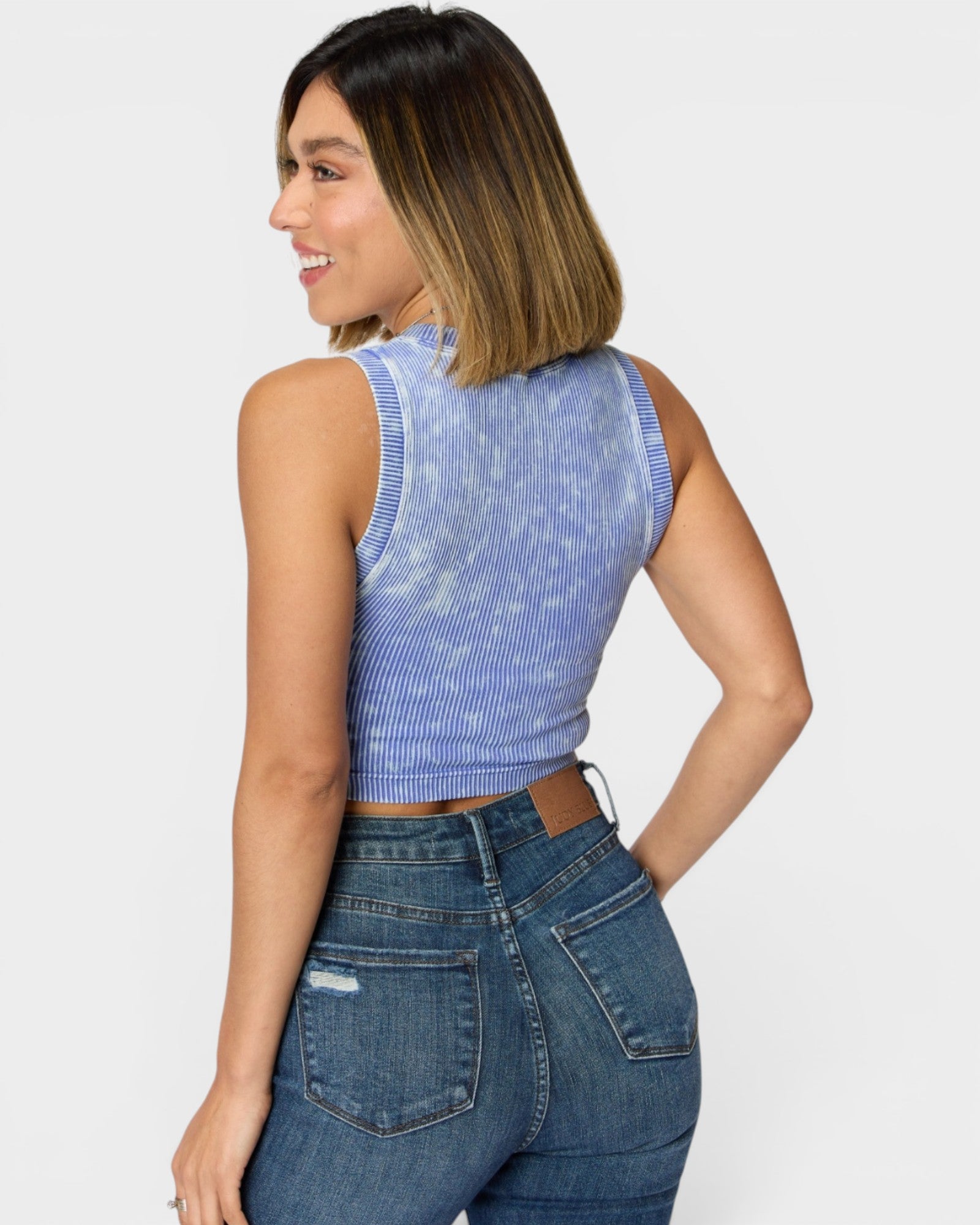 Woman wearing a blue denim sleeveless top and jeans on a white background