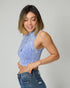 Woman wearing a blue sleeveless top and jeans against a plain background