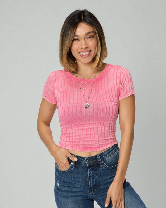 Woman wearing a pink ribbed top and blue jeans on a gray background