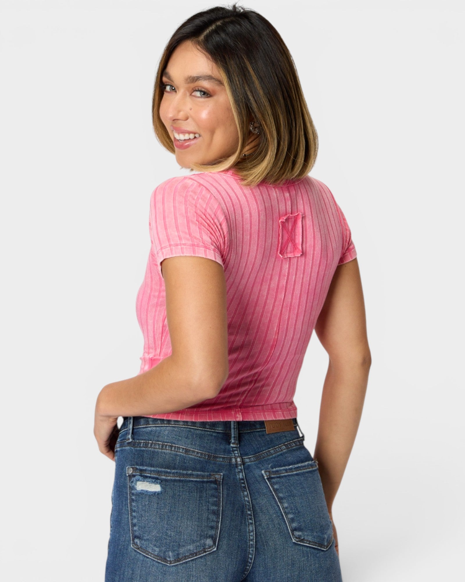 Woman wearing a pink ribbed t-shirt and blue jeans on a white background