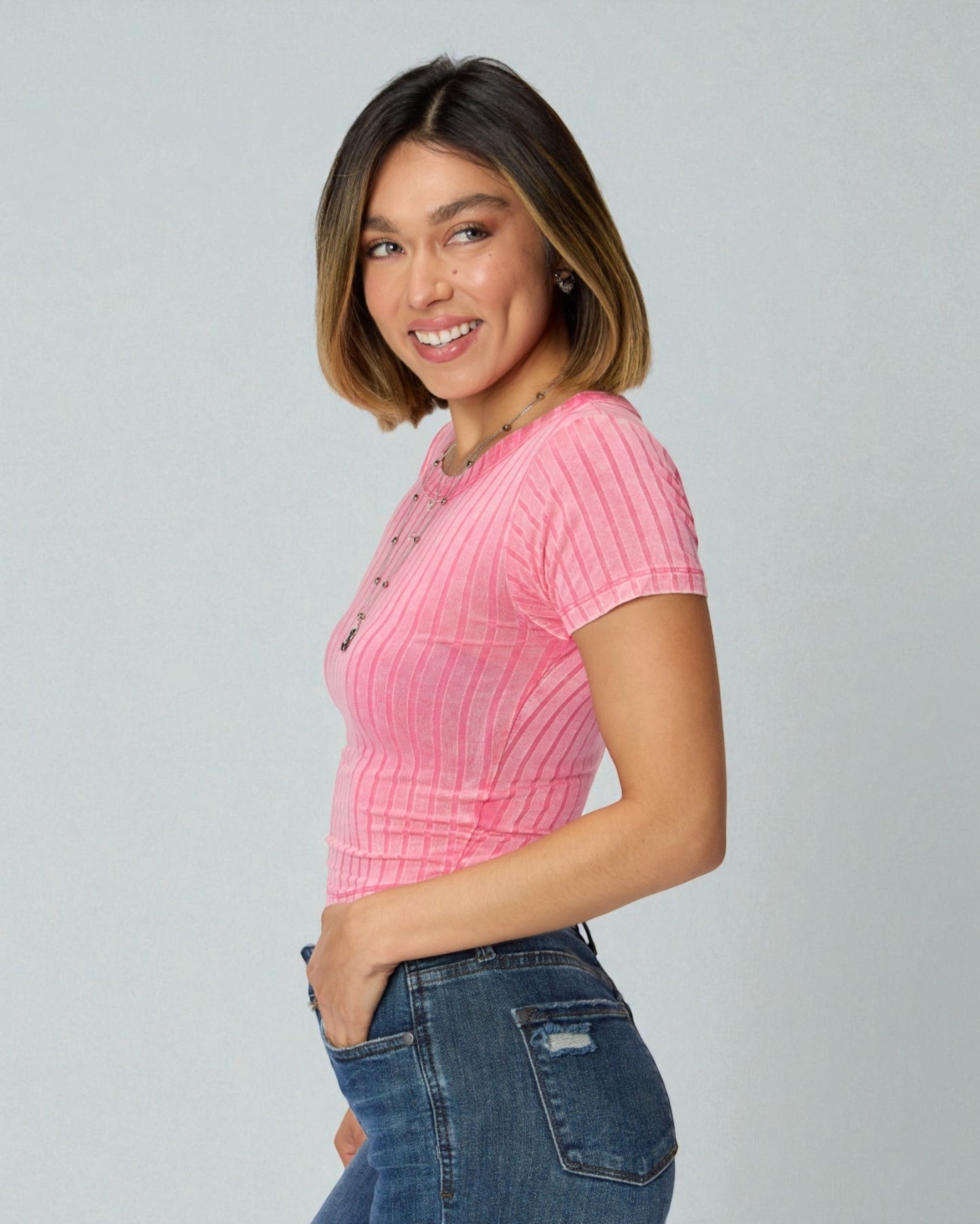 Woman wearing a pink ribbed sweater and blue jeans on a gray background