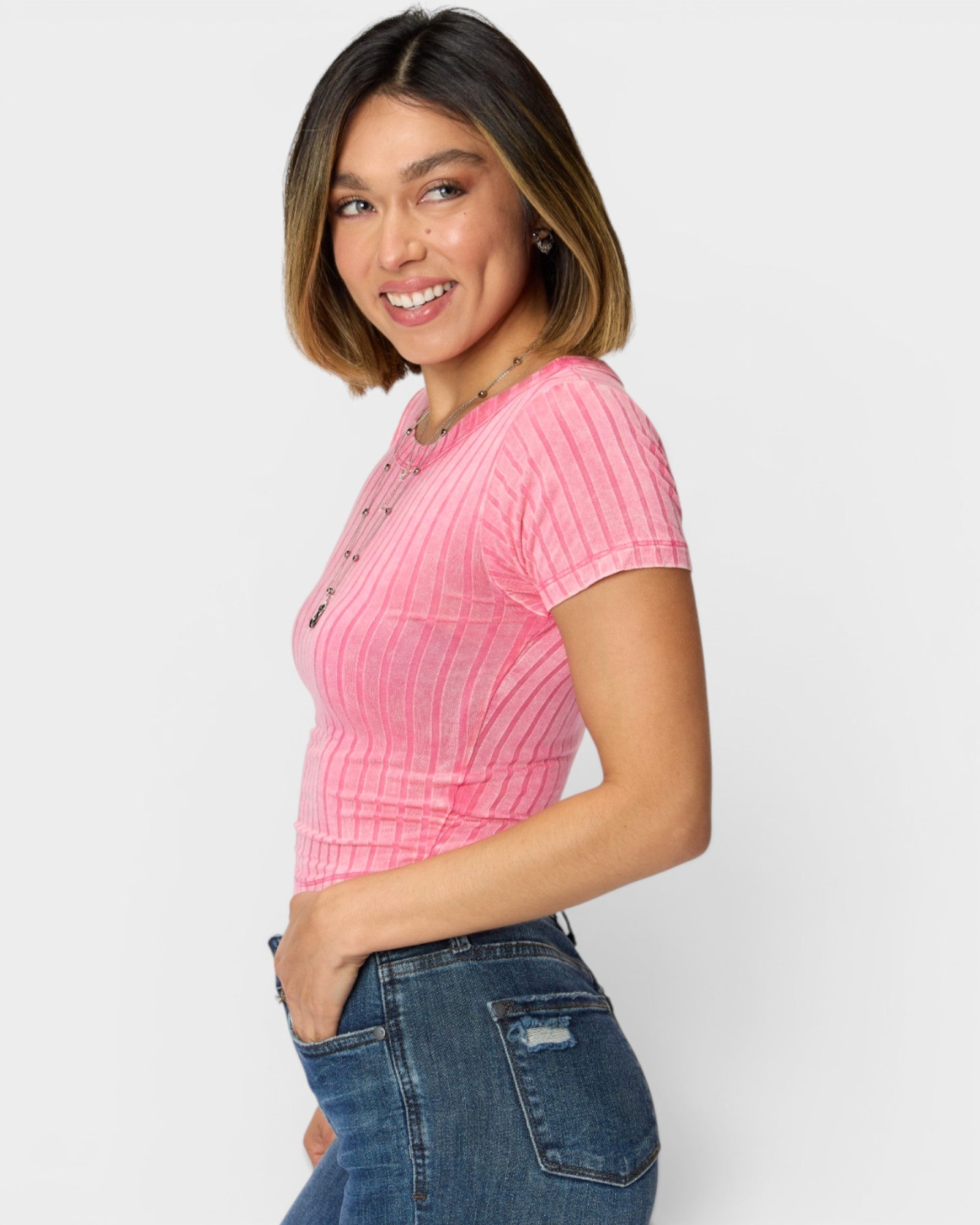 Woman wearing a pink ribbed sweater and blue jeans on a white background