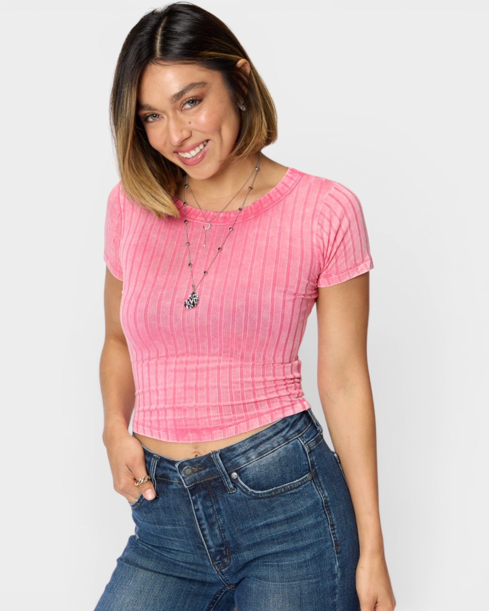 Woman wearing a pink ribbed crop top and blue jeans on a light gray background
