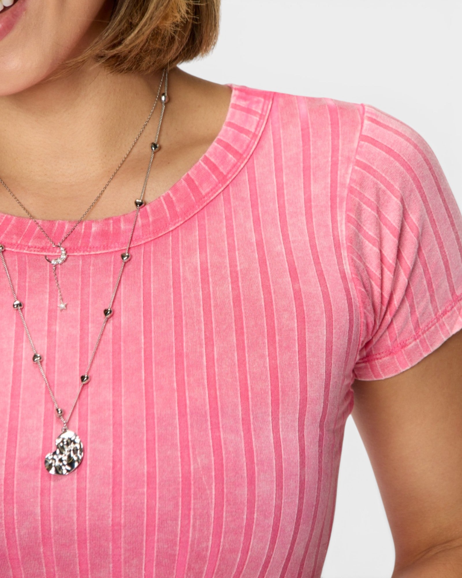 Person wearing a pink shirt with a necklace featuring a heart pendant.