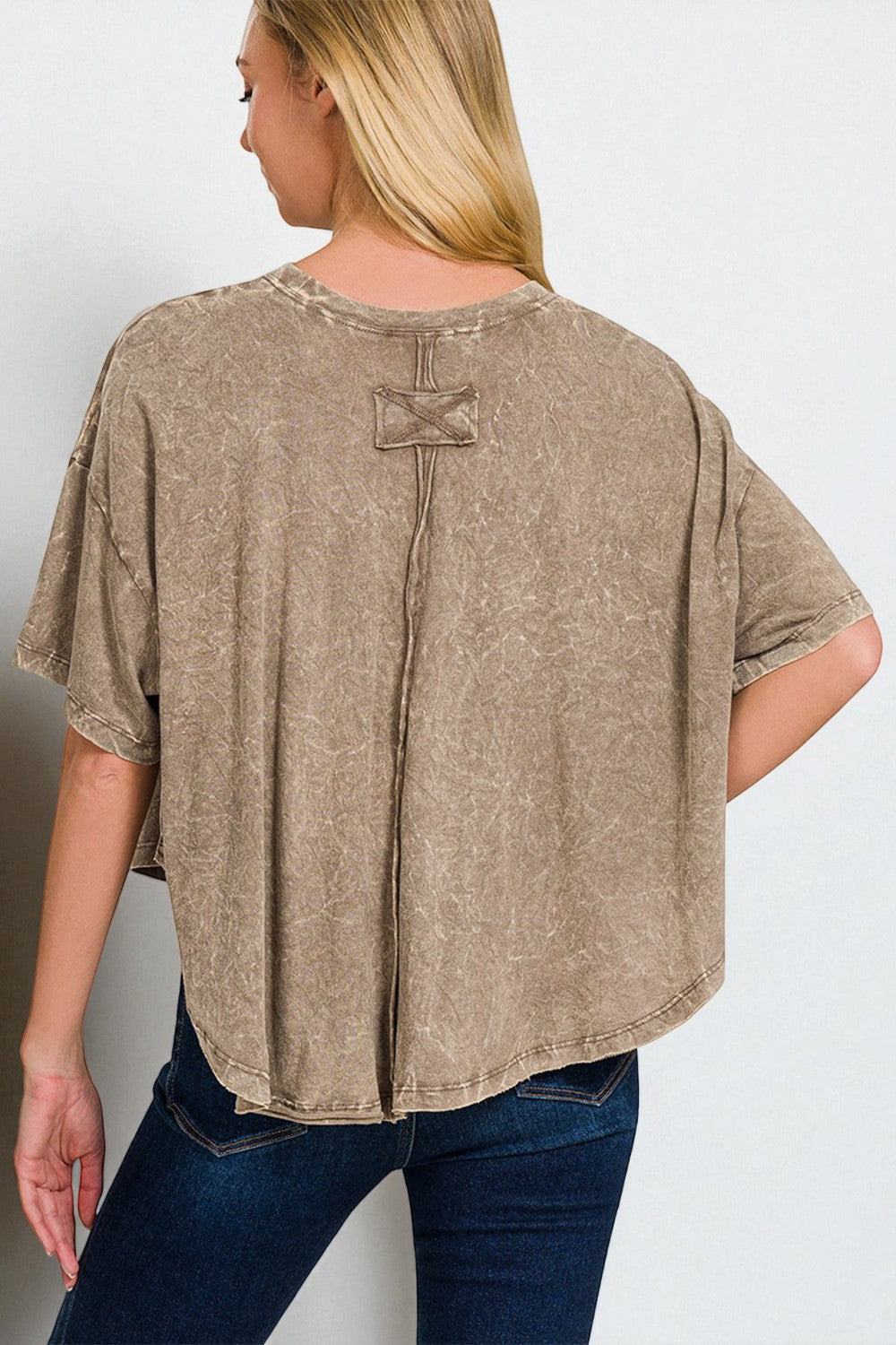 Woman wearing a beige oversized t-shirt with a decorative button on a plain background