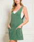 Woman wearing a green sleeveless dress with a white top underneath against a plain background