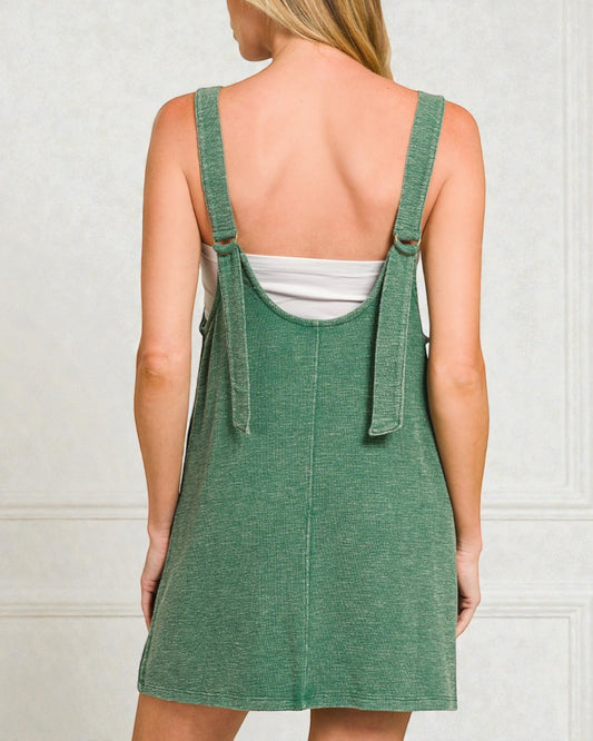 Green denim pinafore dress worn by a person on a plain background