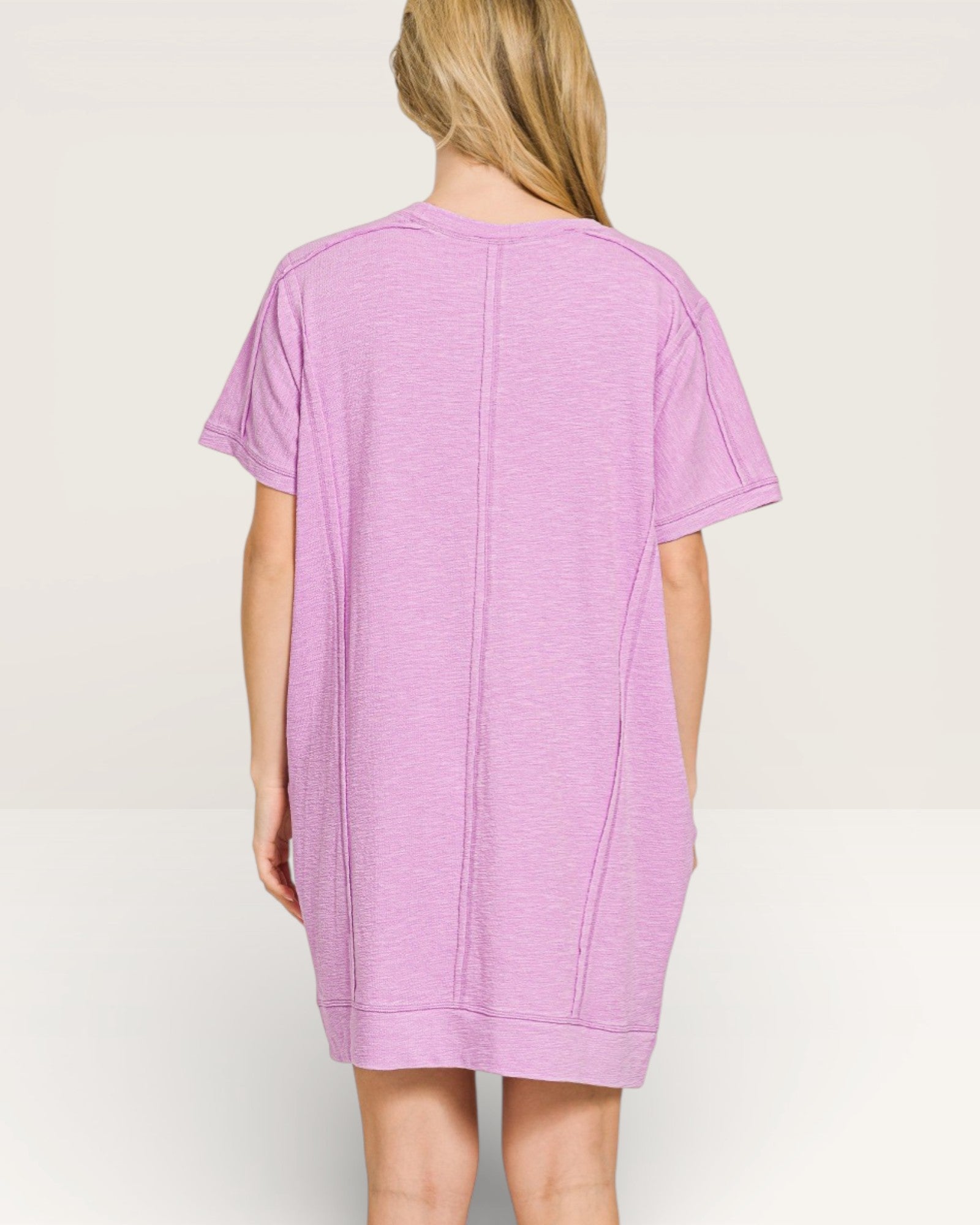 Person wearing a light purple t-shirt dress on a plain background