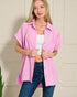 Woman wearing a pink shirt over a white top and blue jeans against a neutral background
