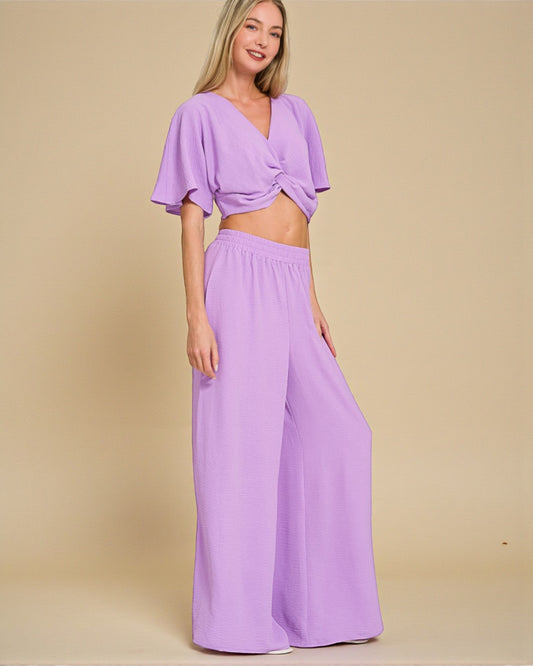 Woman wearing a purple outfit with a top and wide-leg pants on a beige background