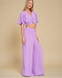Woman wearing a purple outfit with a top and wide-leg pants on a beige background