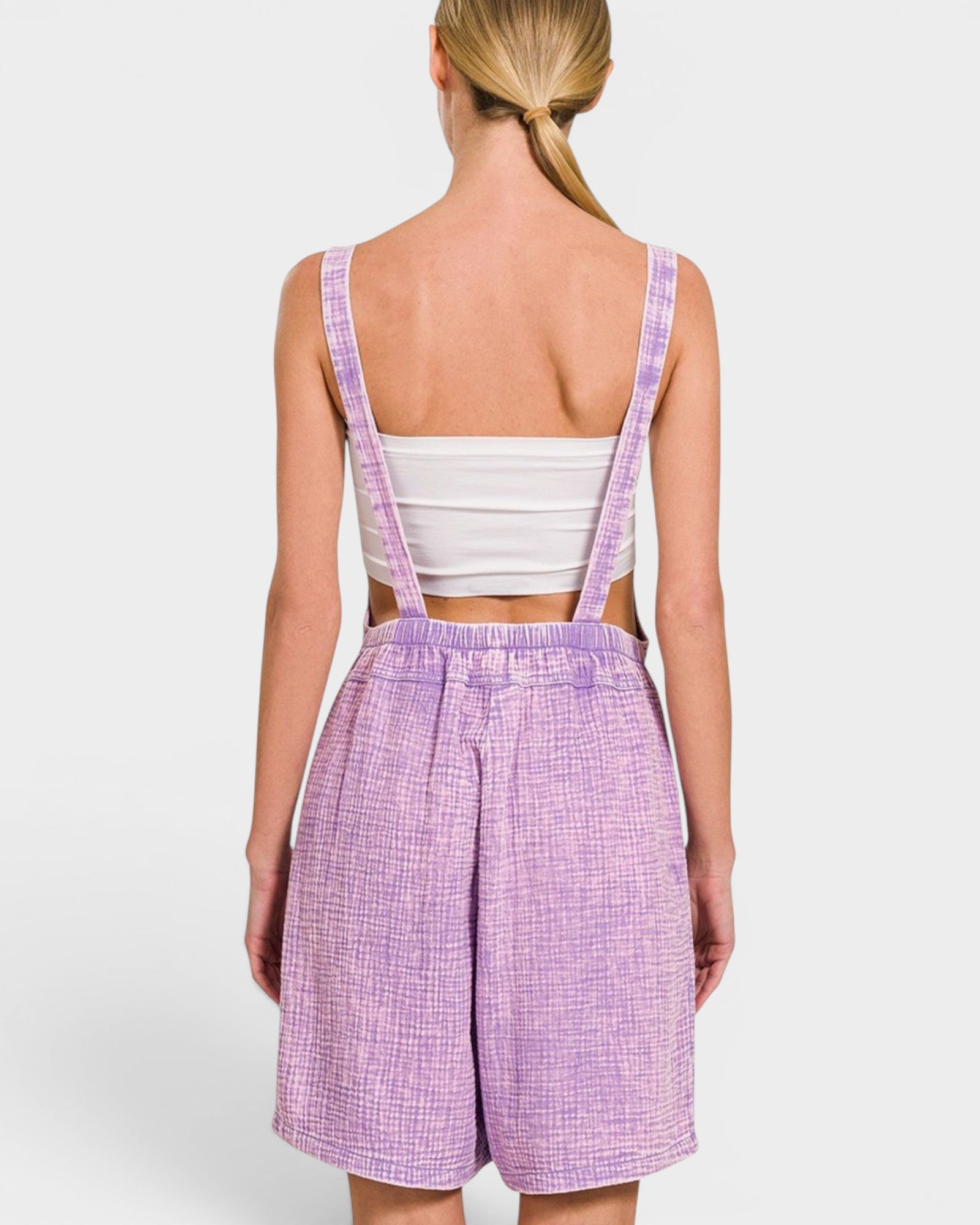 Person wearing a white crop top and purple checkered shorts with suspenders on a white background