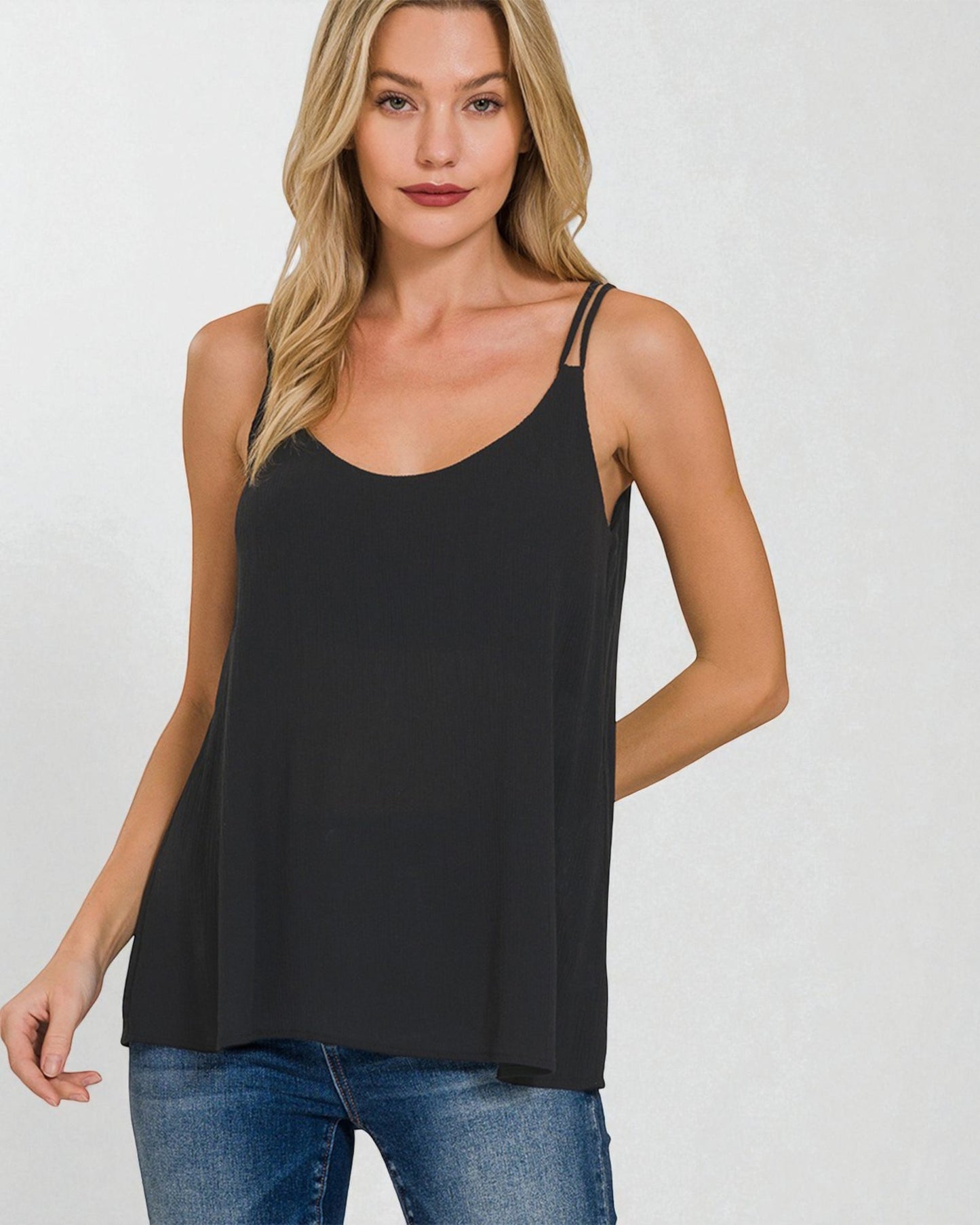 Woman wearing a black tank top and blue jeans on a plain background