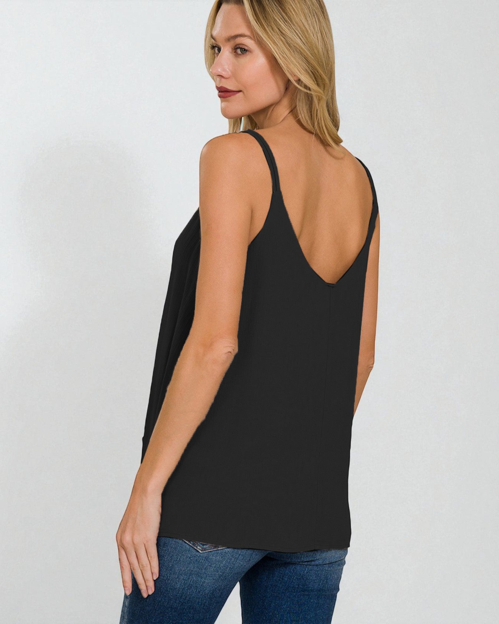 Woman wearing a black tank top and blue jeans on a white background