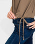 Person wearing a brown top with a tie detail and blue jeans on a light gray background
