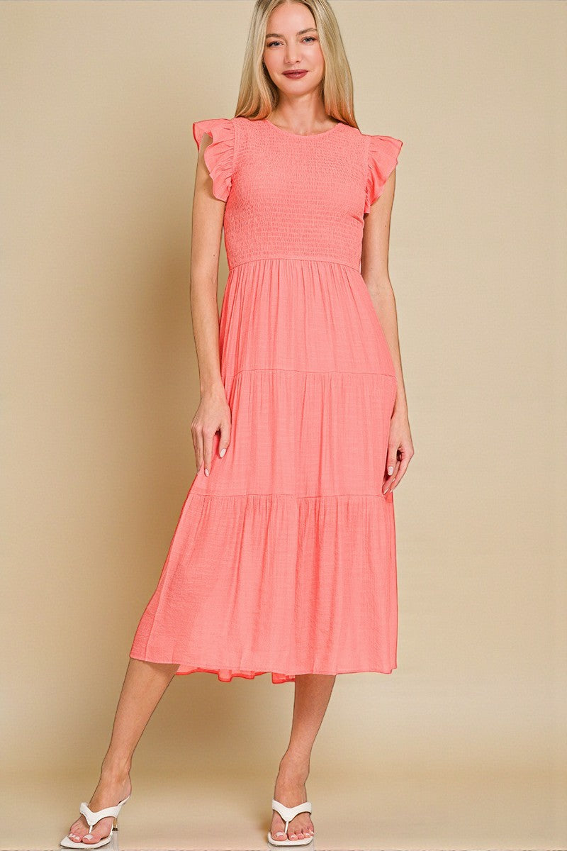 Woman wearing a coral dress with ruffled sleeves against a beige background