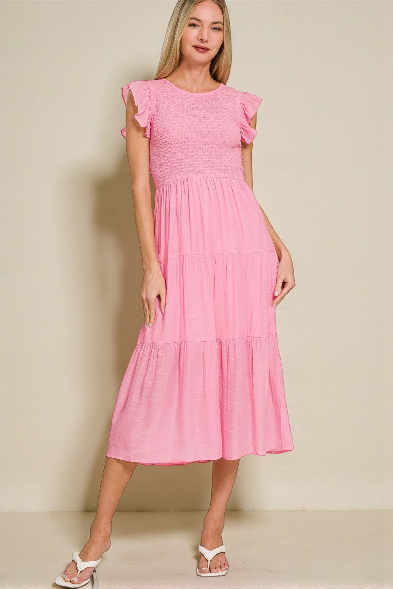 Woman wearing a pink dress with ruffled sleeves against a beige background