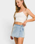 Woman wearing a white crop top and denim skirt on a plain background
