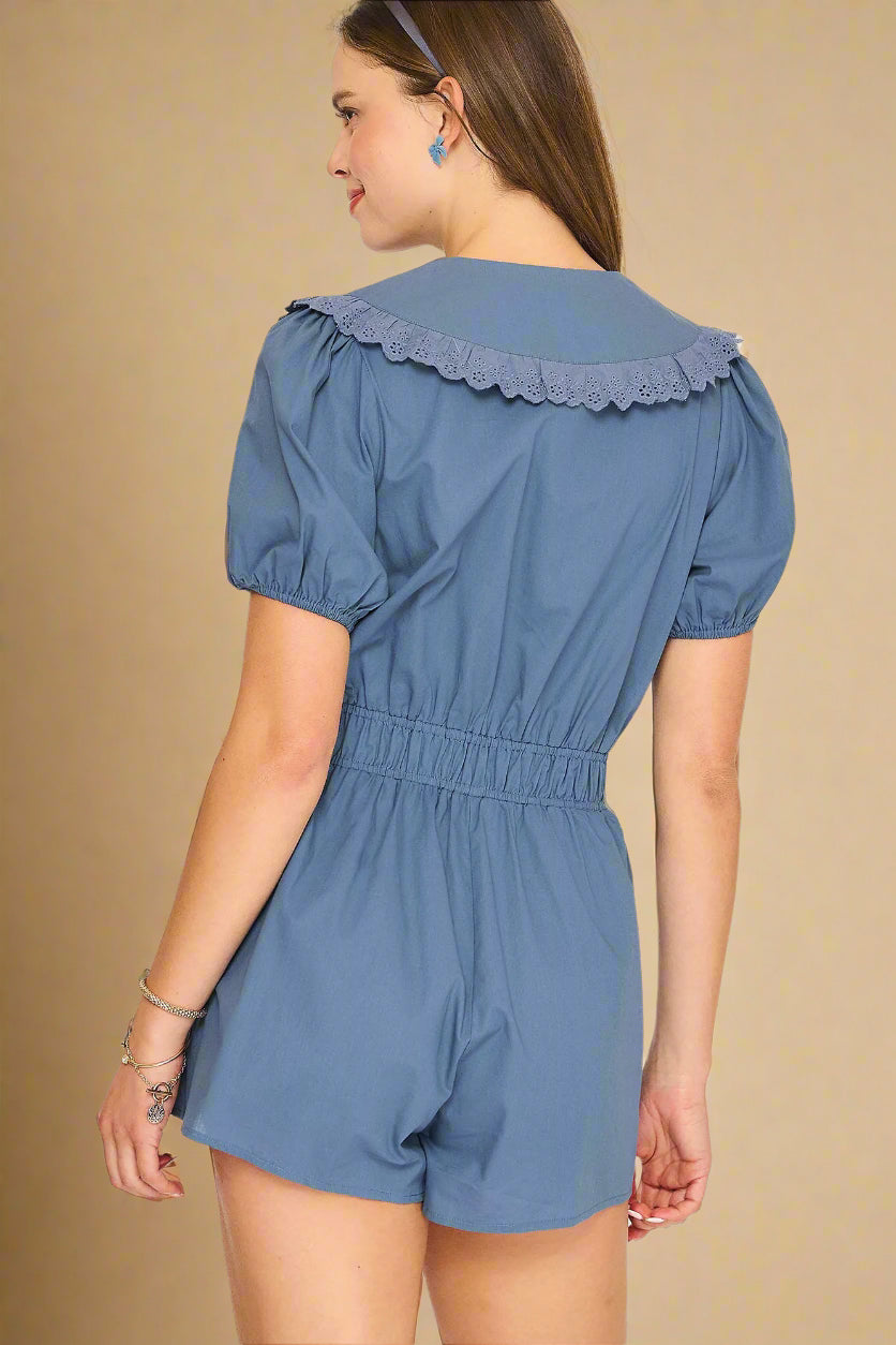 Woman wearing a blue romper with ruffled collar on a light beige background