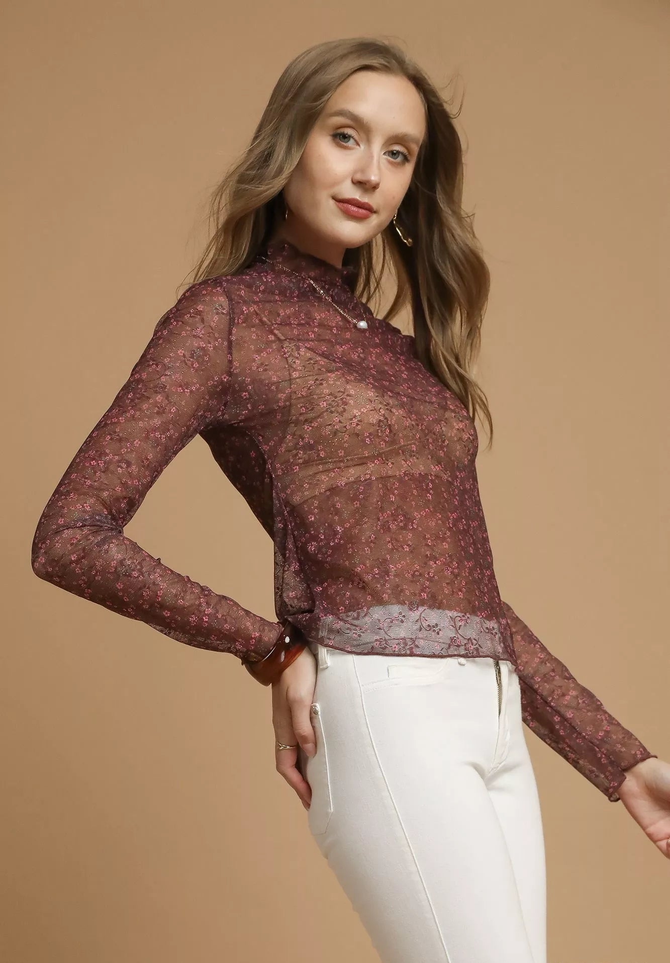 Woman wearing a burgundy lace top and white pants on a beige background