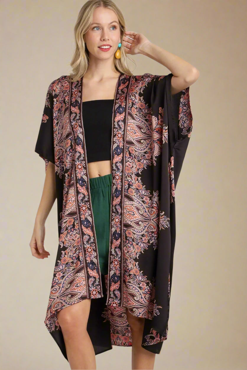 Woman wearing a black and pink patterned kimono over a black top and green pants on a white background.